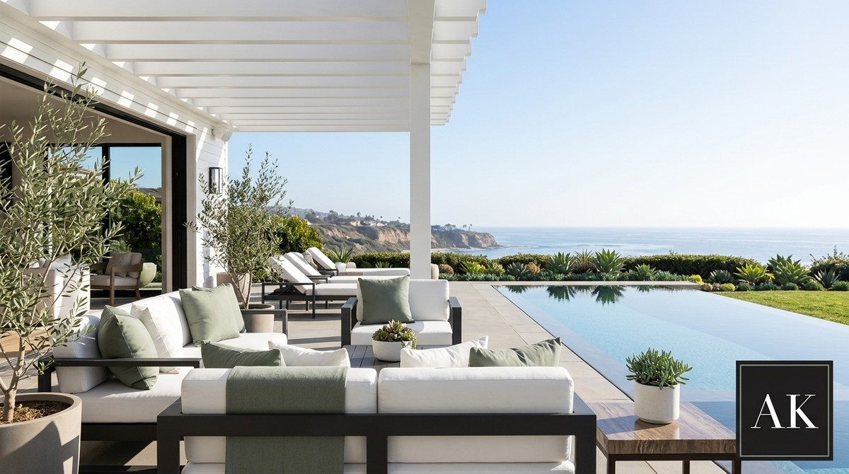Modern patio with white sofas, green pillows, infinity pool, and ocean view, showcasing coastal luxury real estate.